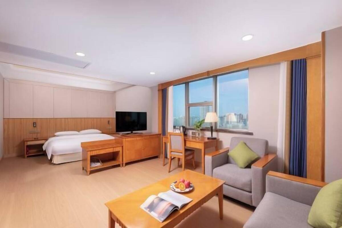Habitación de hotel con cama, escritorio, televisor, sofá y un ventanal grande.