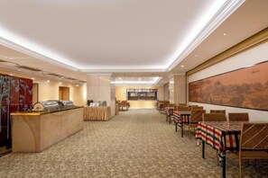 Een hotel lobby met een receptiebalie, een zithoek en een groot schilderij aan de muur.