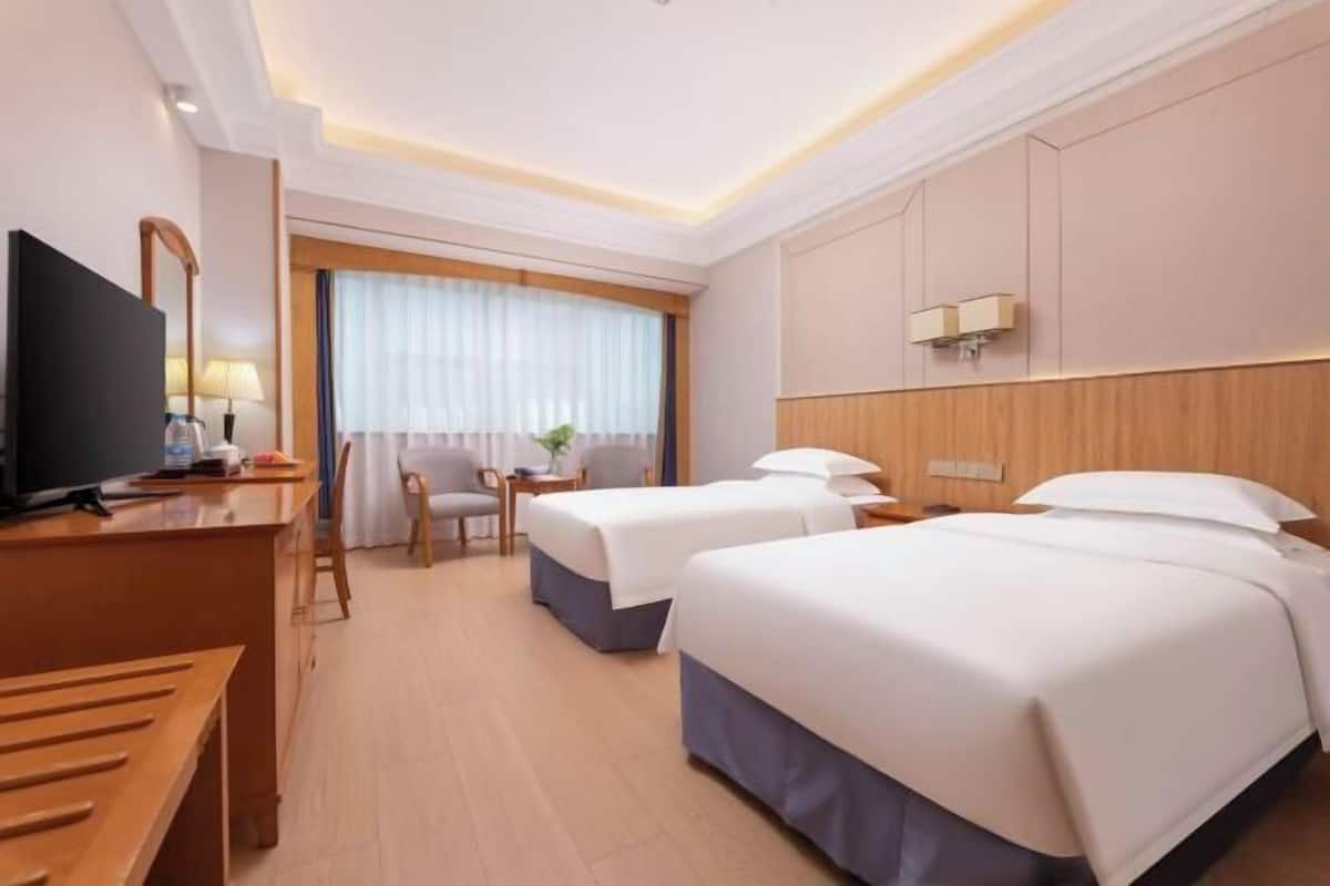 Habitación de hotel con escritorio, dos camas, televisor y ventana con cortinas.