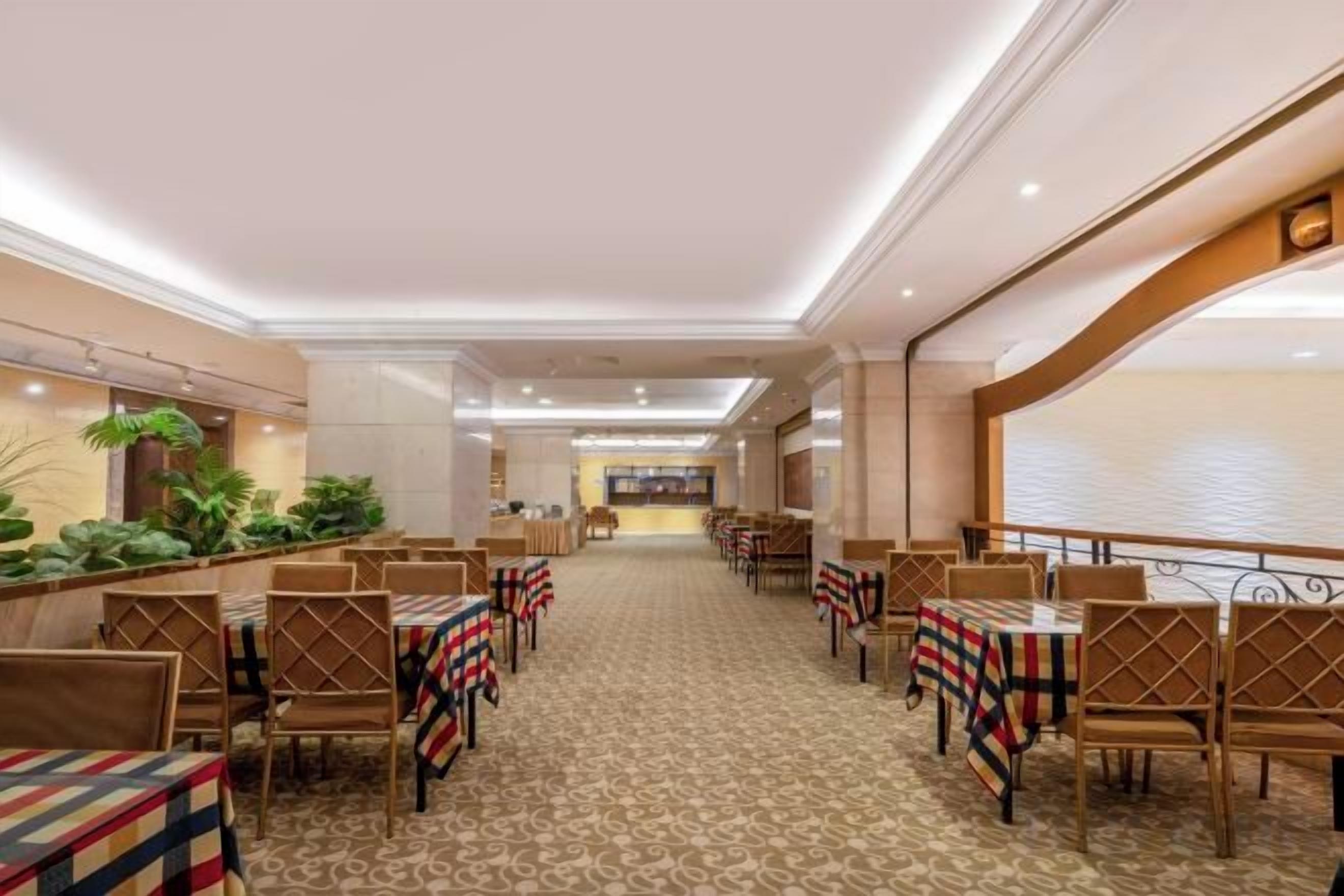 Un comedor de hotel con varias mesas y sillas, una alfombra estampada y vista al vestíbulo.