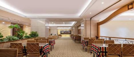 Un comedor de hotel con varias mesas y sillas, una alfombra estampada y vista al vestíbulo.