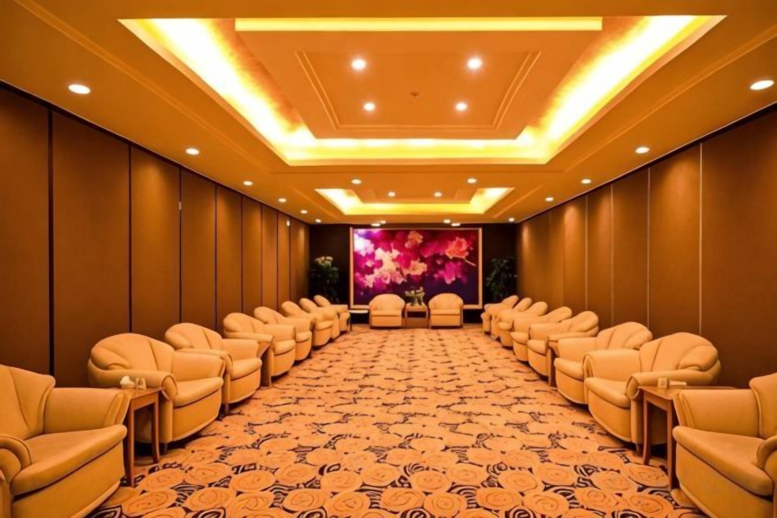 Un salón de conferencias con filas de sillones de cuero, alfombra estampada y un fondo con motivos florales.