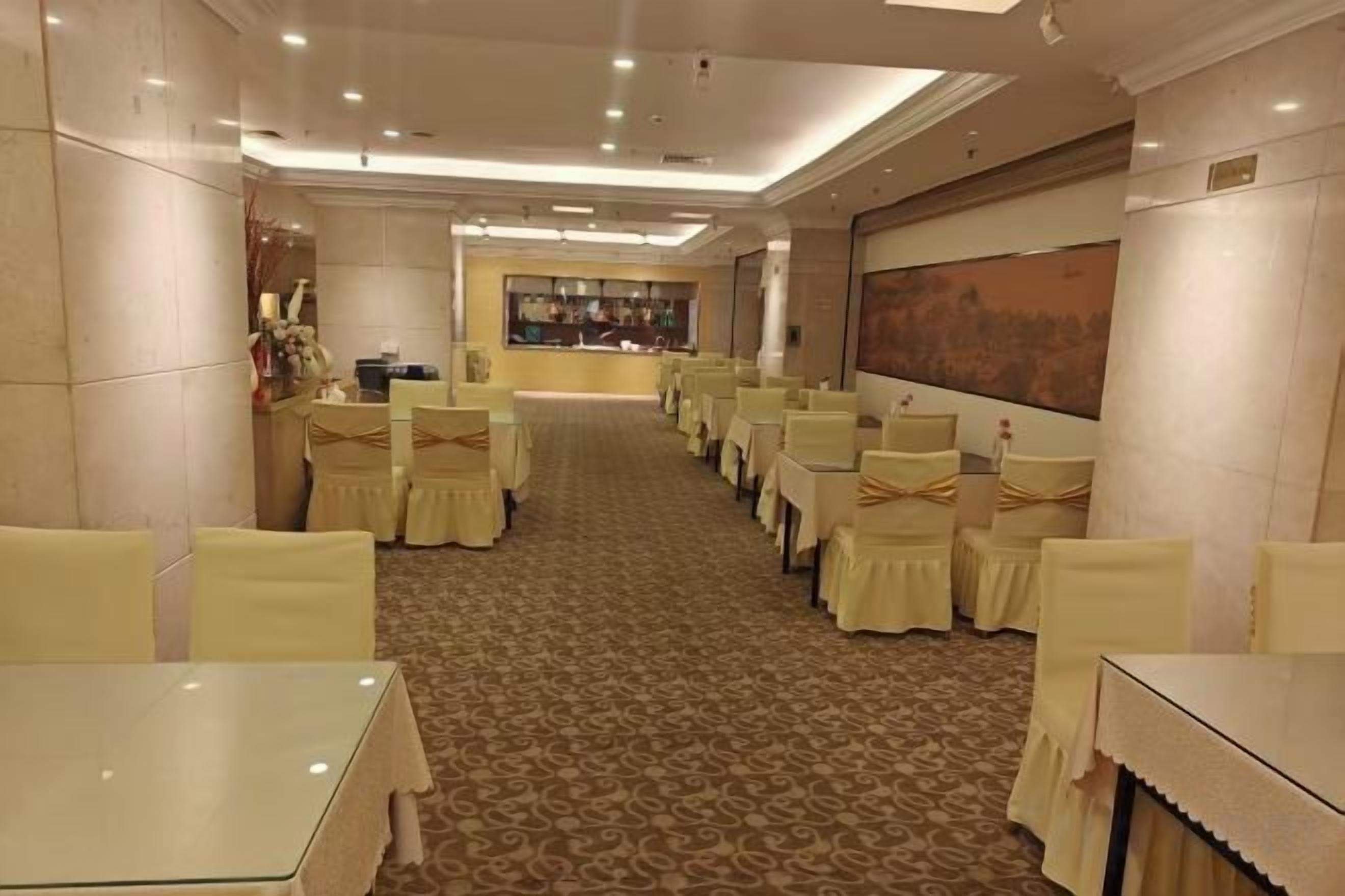 Une salle à manger d’hôtel avec des rangées de tables et de chaises, un sol recouvert de moquette et un grand tableau accroché au mur.