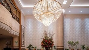 Un vestíbulo con una gran araña, una recepción y un jarrón decorativo con flores.