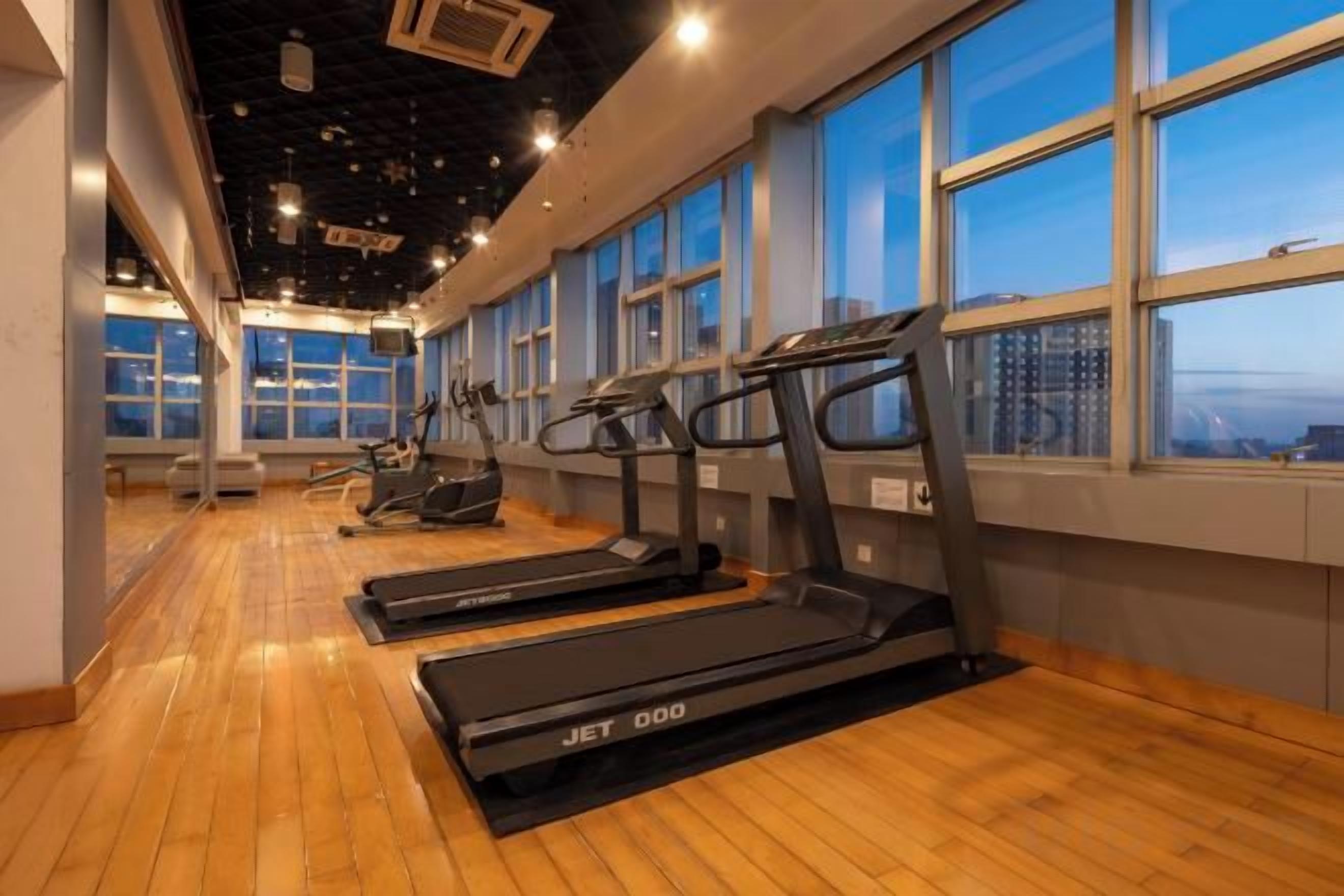 A gym with treadmills, exercise bikes, and a wooden floor.