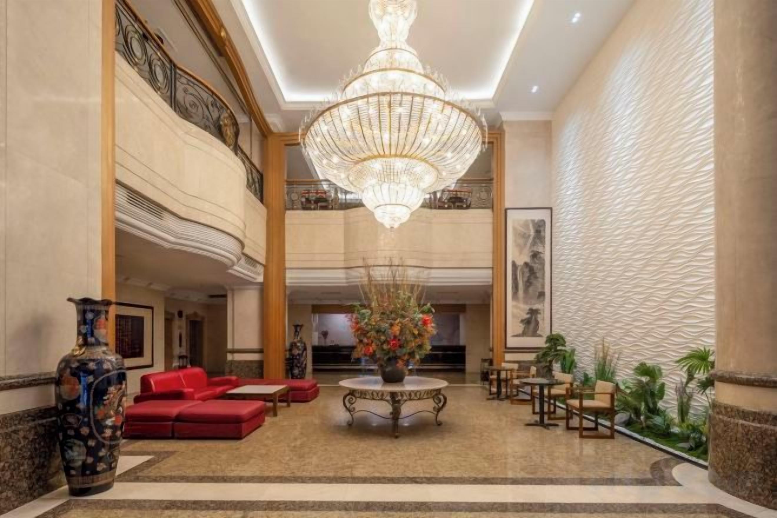 A lobby with a chandelier, red sofas, a table with flowers, and a large wall with a textured pattern.