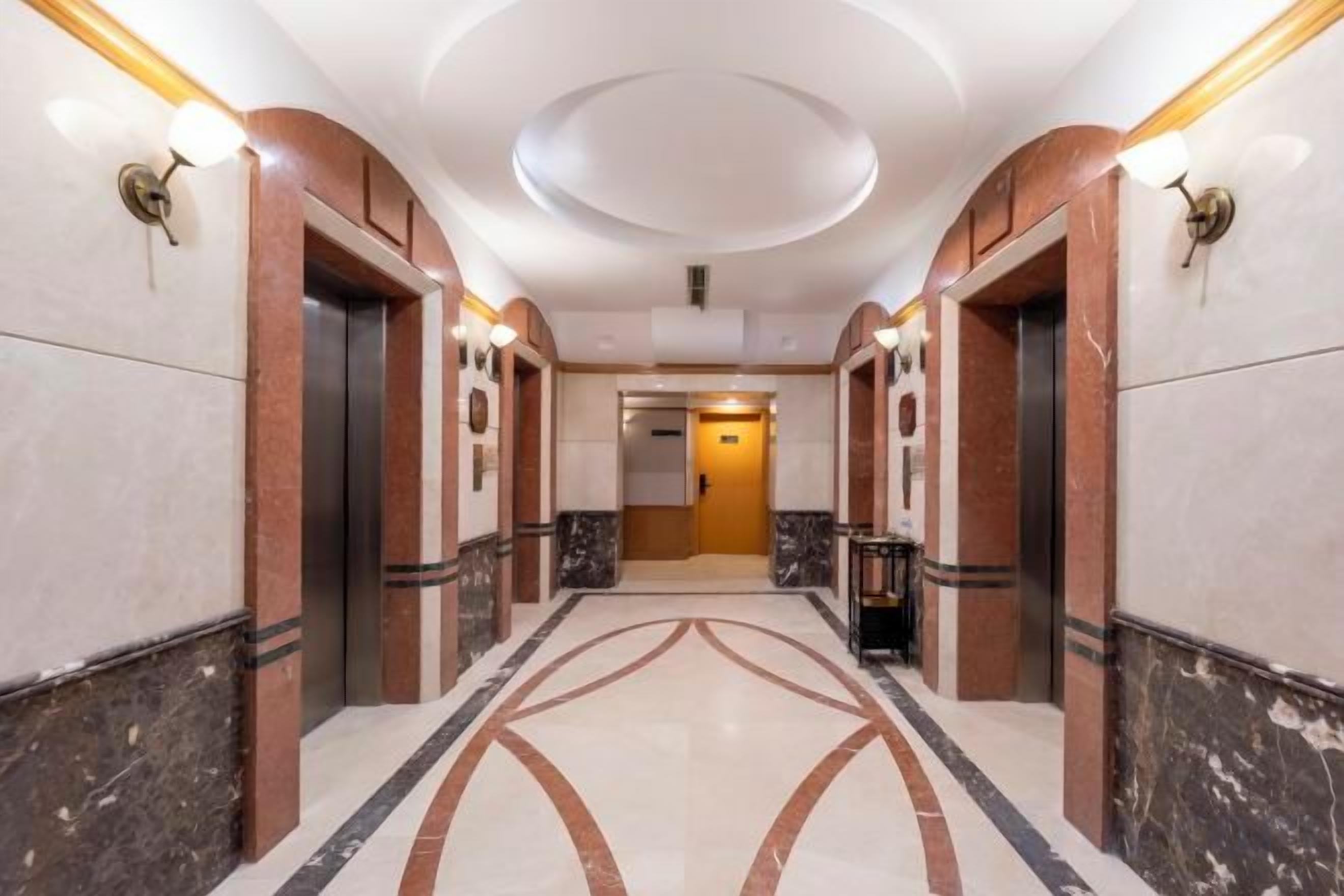 Un pasillo de hotel con piso de mármol, apliques en la pared y un diseño de techo circular.