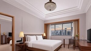 Habitación de hotel con cama, escritorio, silla y un ventanal con vista a la ciudad.