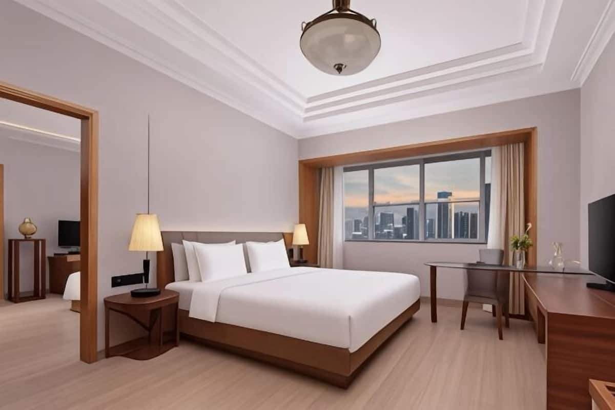 Habitación de hotel con cama, escritorio, silla y un ventanal con vista a la ciudad.