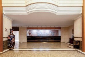 Un hall con mostrador de recepción, un jarrón grande y un mural en la pared.