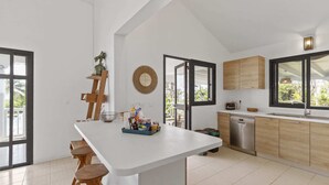 A modern kitchen with a central island, wooden stools, a built-in dishwasher, and large windows. - Villa 3 Anses - Three Bedroom Villa, Sleeps 8 (Sainte-Anne)