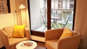 Una sala de estar moderna con un sofá y un sillón, una pequeña mesa redonda y un ventanal con vistas a un balcón exterior.