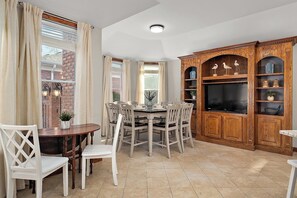 A dining area with a brick wall, a wooden TV stand, and a dining table with chairs. - Mins to Golf & Ocean City! Sleeps 16 w. Game Room! (Berlin)