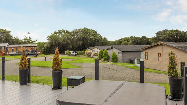 A deck with a large, dark-colored sofa and potted plants, overlooking a residential area with houses and a driveway.