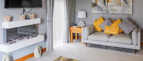 Un salon moderne doté d’un téléviseur à écran plat, d’un canapé gris agrémenté de coussins jaunes et gris, et d’un grand tableau abstrait accroché au mur.