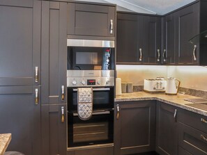 Une cuisine moderne avec des meubles de rangement aux couleurs sombres, un four encastré, un four à micro-ondes et un grille-pain posés sur le plan de travail.