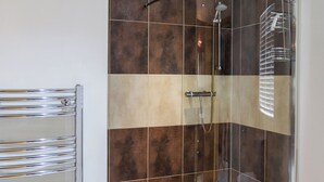 Een moderne badkamer met een douchecabine van glas, een chromen handdoekhouder en een betegelde wand met een combinatie van bruine en beige tegels.