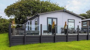 A modern mobile home with a covered patio, large windows, and a fenced outdoor area.