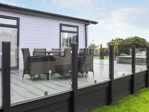 Une terrasse extérieure couverte, avec une table et des chaises, une terrasse en bois et un bâtiment blanc en arrière-plan.