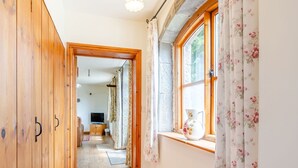 A hallway with wooden flooring, a television in the background, and floral curtains on the windows.