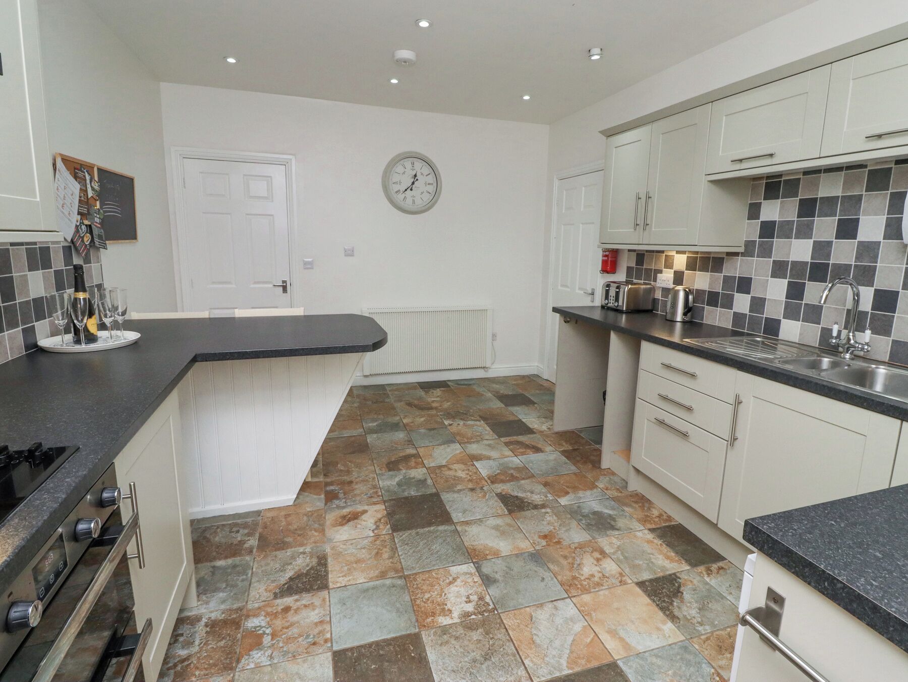 A modern kitchen with white cabinetry, a black countertop, and a tiled floor.
