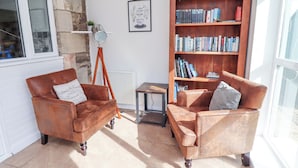 Ein gemütliches Zimmer mit zwei braunen Ledersesseln, einem Bücherregal aus Holz und einem gerahmten Zitat an der Wand.