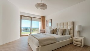 A modern bedroom with a large bed, a nightstand, a lamp, and a view of the outdoors.