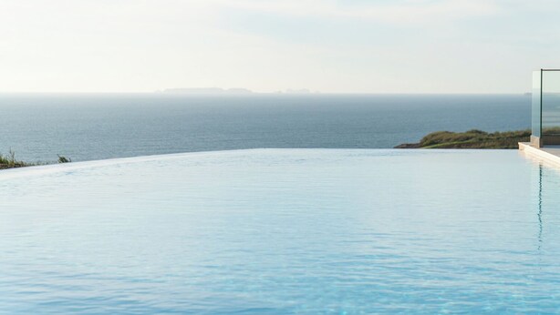 A modern infinity pool with a clear view of the ocean and distant land.