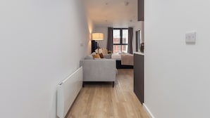 A narrow hallway with a grey sofa, a lamp, and a bed in the background. - City Living Studio - Studio Apartment, Sleeps 2 (Manchester)