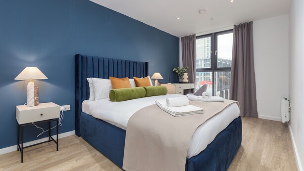 A modern hotel room with a large bed, a nightstand, a desk, and a window with curtains.