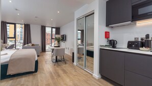 Et moderne hotelværelse med seng, skrivebord, stol, fjernsyn og et tekøkken med mikroovn, samt en skydedør til en balkon.