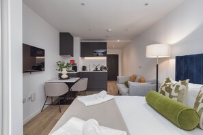 A modern hotel room with a bed, a desk, a chair, a sofa, a lamp, and a kitchenette. - Chic New Cross Studio (Manchester)