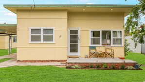 A single-story house with a flat roof, a front door, and two windows. - Coastal Retro House by Book Jervis Bay - Husky (Huskisson)