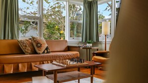 A cozy living room with a brown leather sofa, a chessboard, and a lamp. - Coastal Retro House by Book Jervis Bay - Husky (Huskisson)