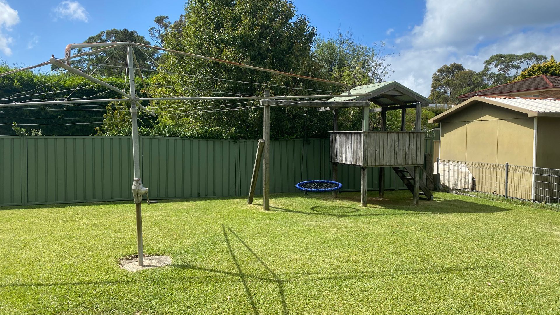 A backyard with a trampoline, a wooden playhouse, and a metal fence.