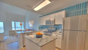 A modern kitchen with white cabinets, a granite countertop, a stainless steel refrigerator, and a microwave. - NEW! Beachside Bliss in Orange Beach (Orange Beach)