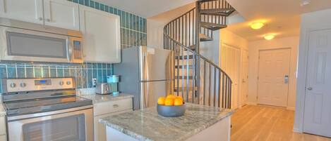 A kitchen with a microwave, stove, refrigerator, and a bowl of oranges on the counter.