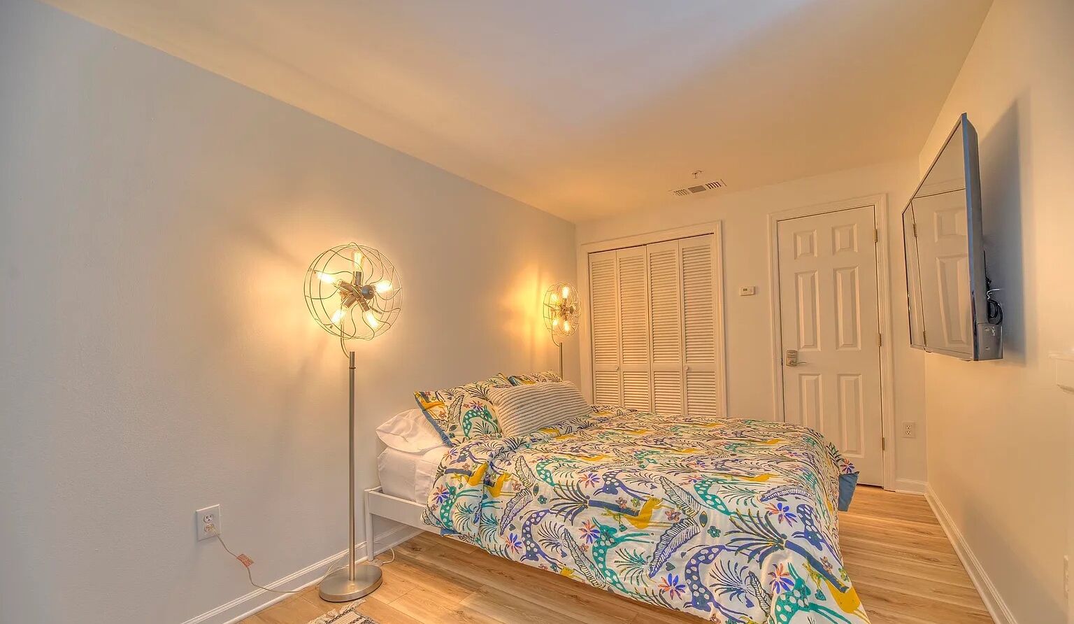 Un dormitorio con una cama, dos lámparas de noche, un armario blanco y una puerta.