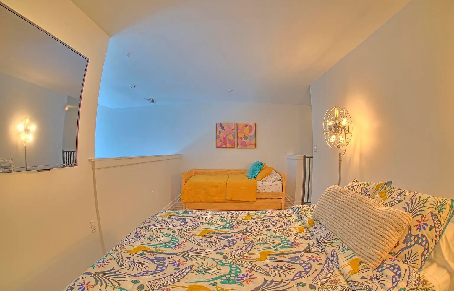 A bedroom with a bed, a bedside table, a mirror, and a wall-mounted light fixture.
