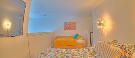 A bedroom with a bed, a bedside table, a mirror, and a wall-mounted light fixture.