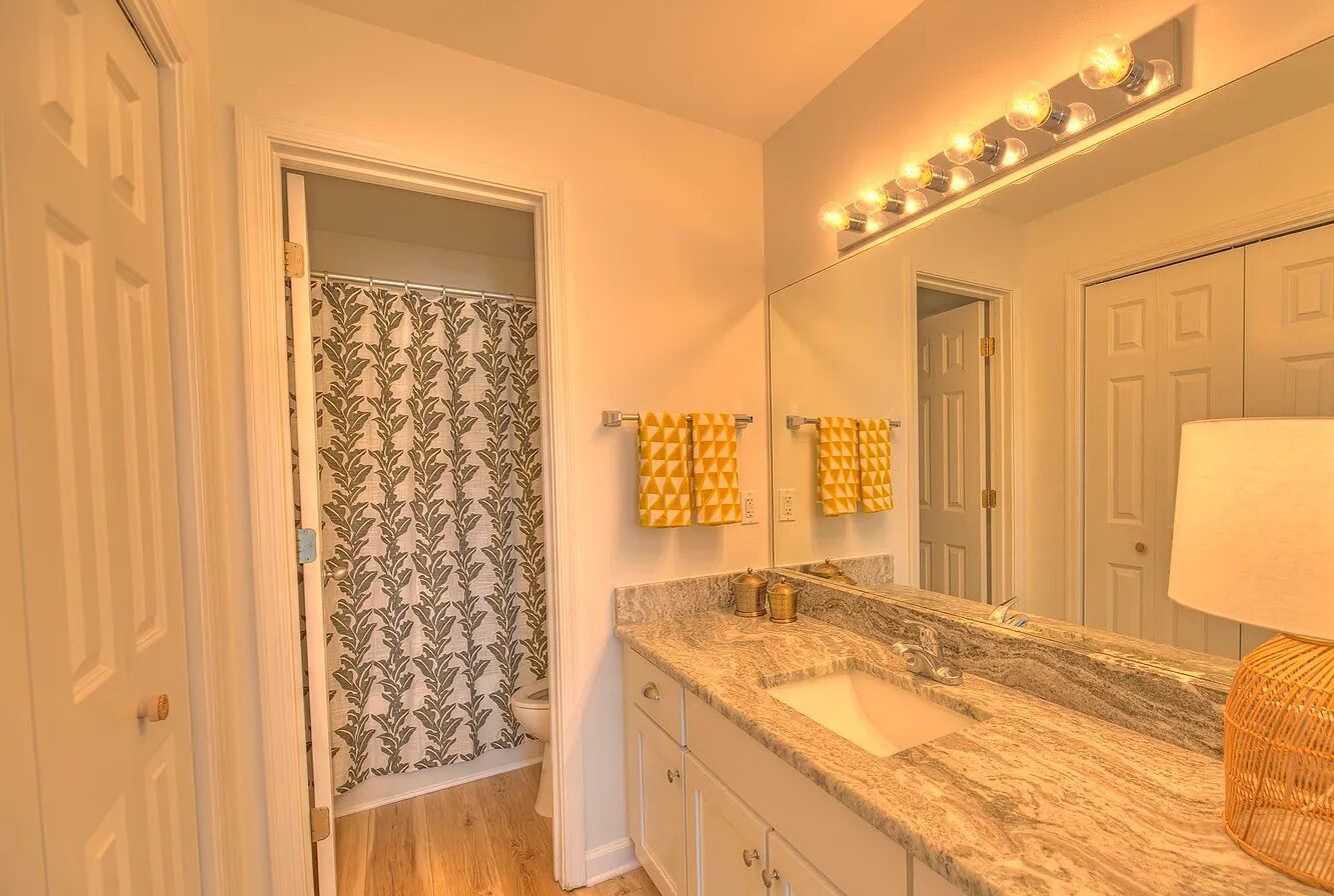 Un baño con tocador, lavabo, espejo con luces y papel tapiz estampado.