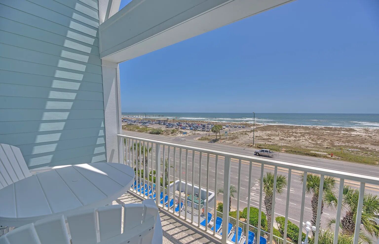 Un balcon offrant une vue sur la plage et l’océan, avec des rampes blanches et des chaises bleues.