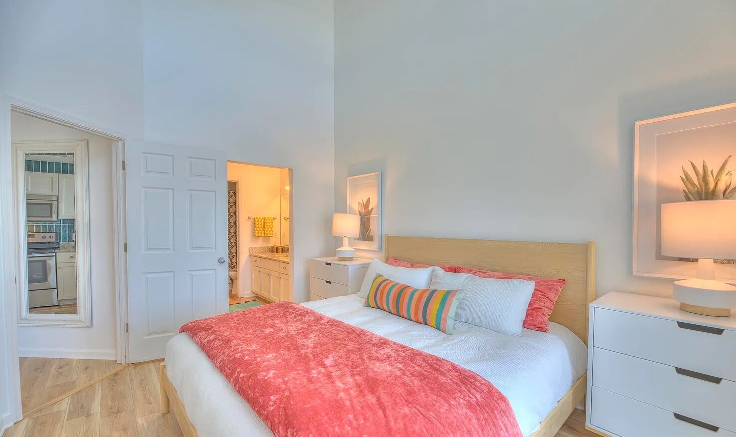 Un dormitorio con una cama, mesitas de noche, un espejo y una puerta que da a la cocina.