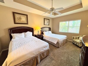A hotel room with two beds, a ceiling fan, a window with blinds, and a couch.
