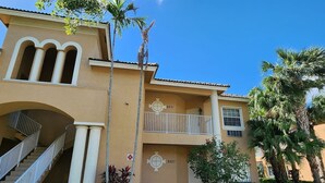 A two-story building with a balcony, a staircase, and a palm tree.