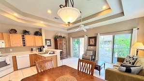 A modern kitchen with wooden cabinets, a dining table with chairs, a ceiling fan, and a view of the outdoors through a sliding glass door.