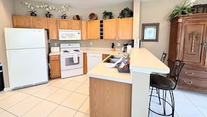 A modern kitchen with wooden cabinets, a white refrigerator, an oven, a microwave, and a sink.