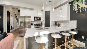 A modern kitchen with white cabinets, stainless steel appliances, and a central island with bar stools. - Toast & Groove - Sleeps 16 - HTX (Houston)