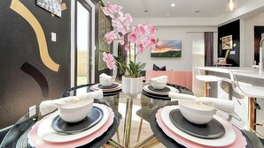 A modern dining area with a glass table set for four, surrounded by black and pink plates and bowls. - Toast & Groove - Sleeps 16 - HTX (Houston)