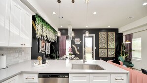 A modern kitchen with white cabinetry, a stainless steel dishwasher, and a central island with a sink. - Toast & Groove - Sleeps 16 - HTX (Houston)